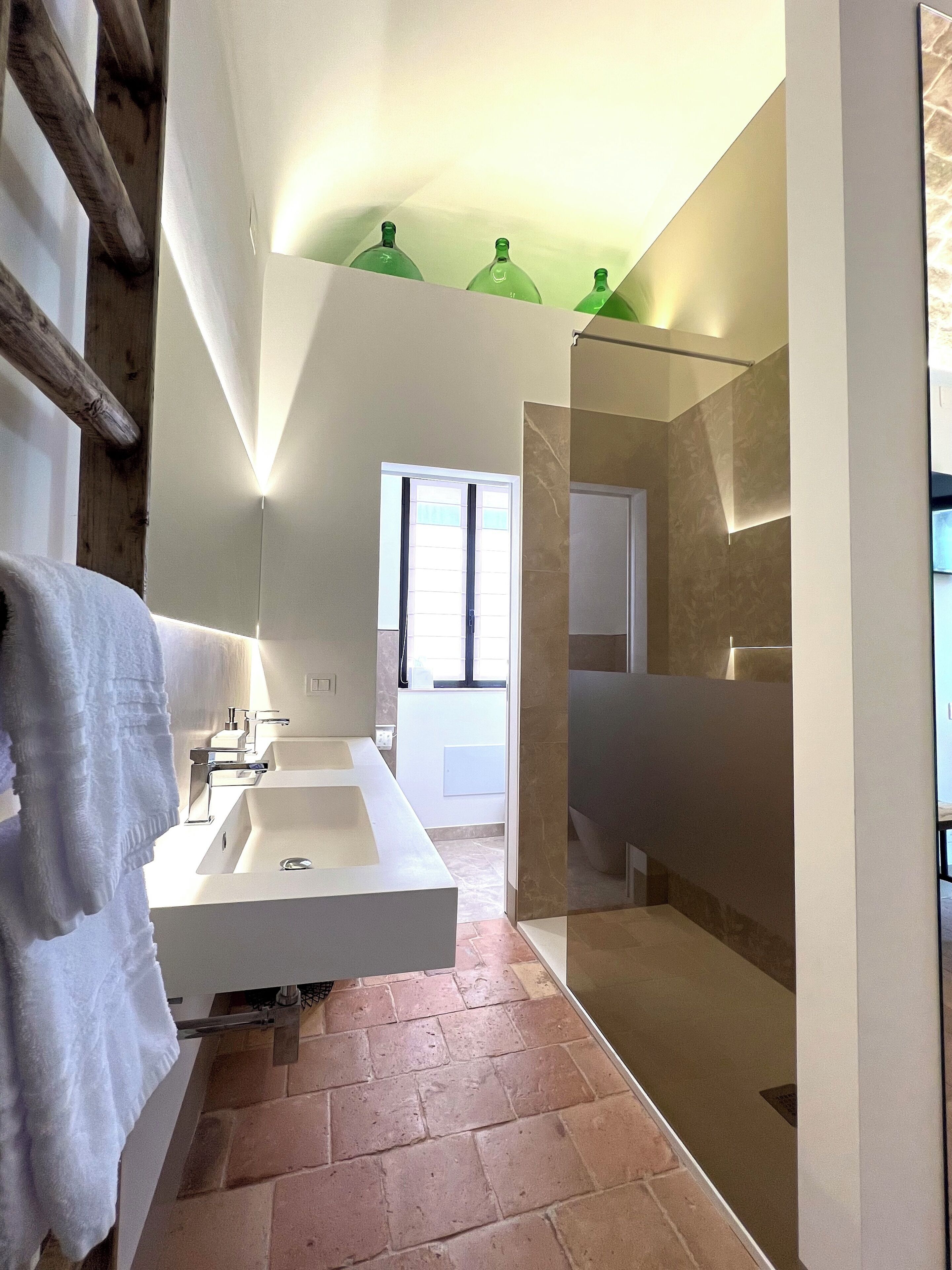 Un baño moderno con un lavamanos grande de color blanco, cabina de ducha con paredes de vidrio y una ventana.