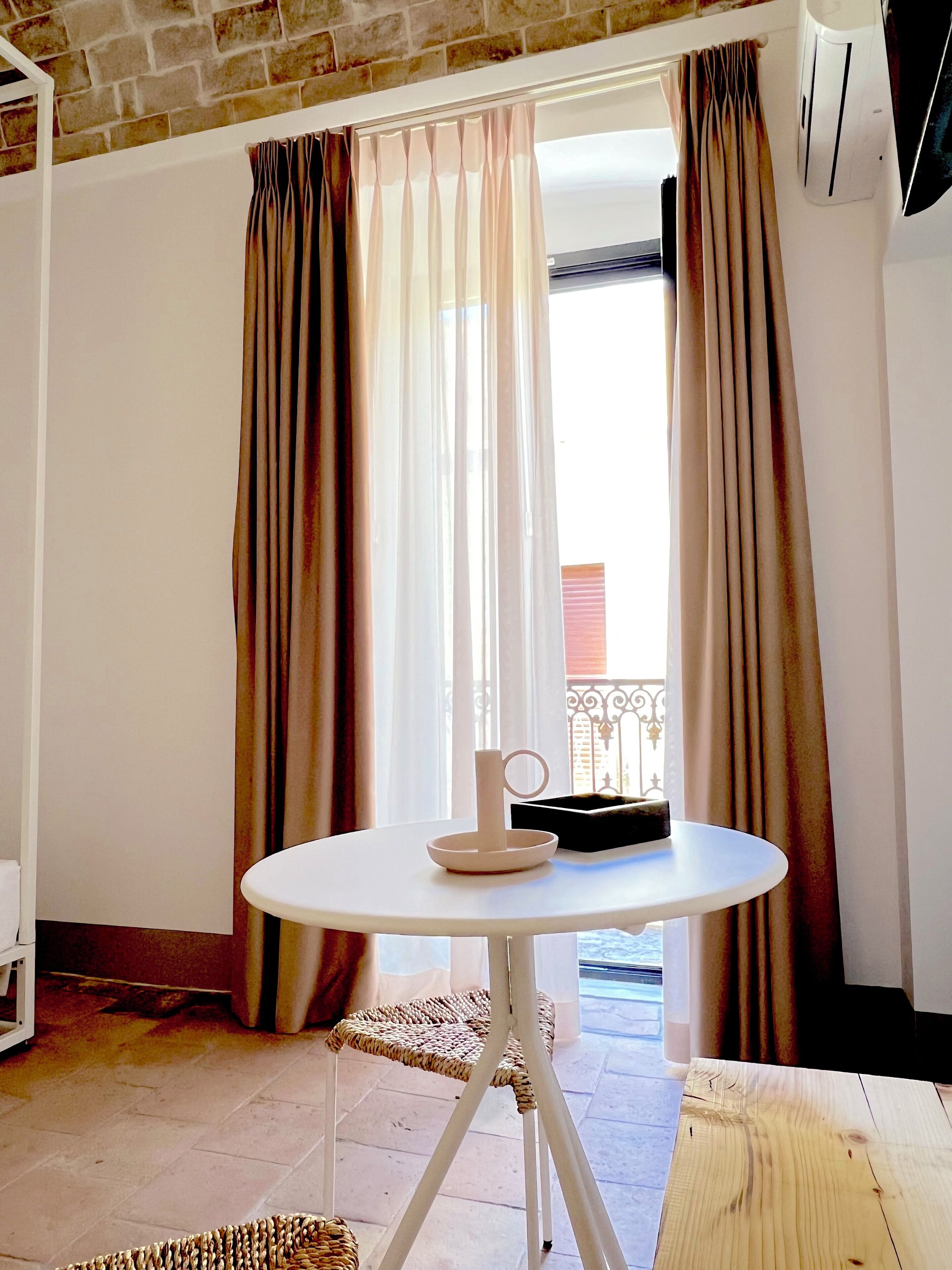 A room with a round white table, a wicker chair, and a window with curtains.