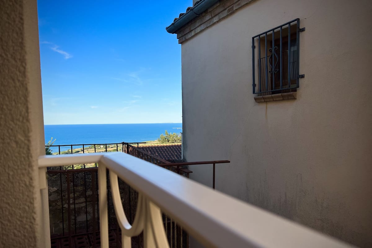 A balcony with a view of the sea and a building with a window.