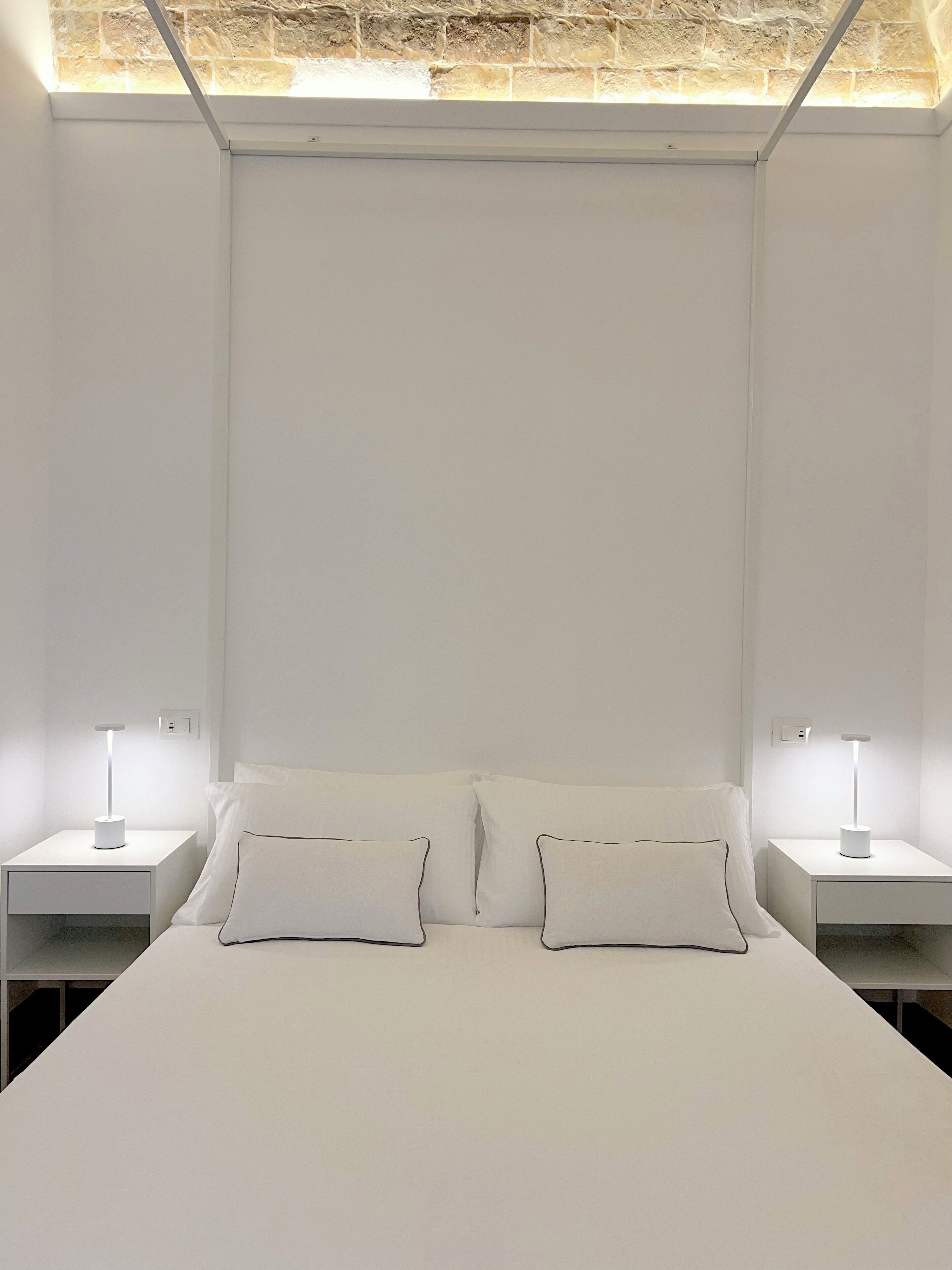 A minimalist bedroom with a large bed, two bedside tables with lamps, and a skylight above.