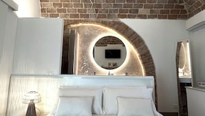 A modern bedroom with a brick ceiling, a circular mirror, a bed with white linens, and a bedside table with a lamp. - RESIDENZA ORTENSIA (Petacciato)