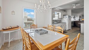 Een eetgedeelte met een witte tafel, houten stoelen, een kroonluchter en uitzicht op de keuken.