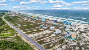 Luchtbeeld van een kustgebied met een weg die langs het strand kronkelt, diverse gebouwen met blauwe daken en een helder uitzicht op de oceaan.