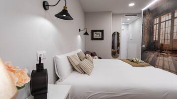 Ein modernes Hotelzimmer mit einem großen Bett, einem Nachttisch mit Lampe, einem gerahmten Bild an der Wand und einem Wandgemälde an der angrenzenden Wand.