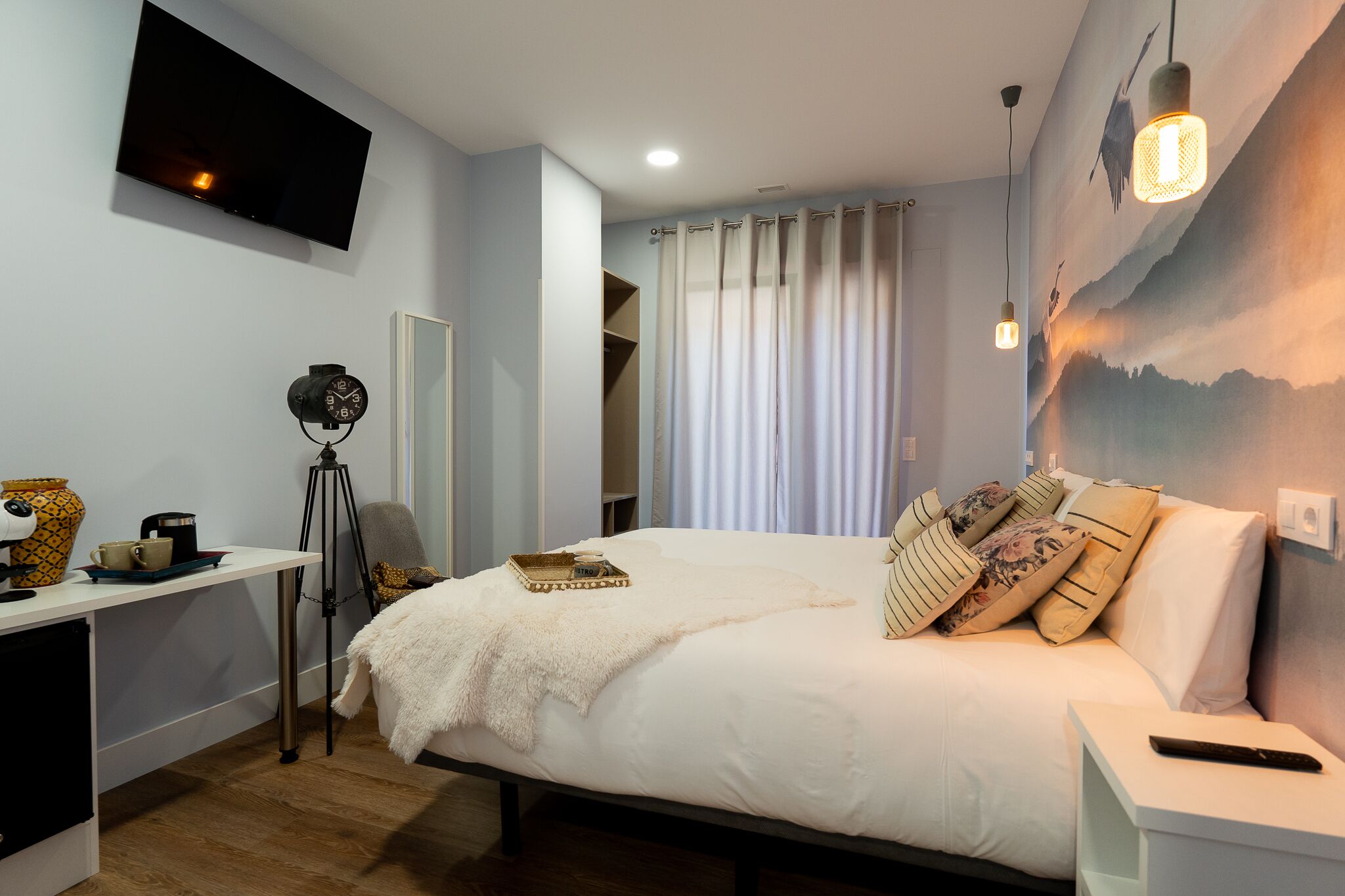 Un dormitorio con cama, mesita de noche, lámpara y televisor montado en la pared.