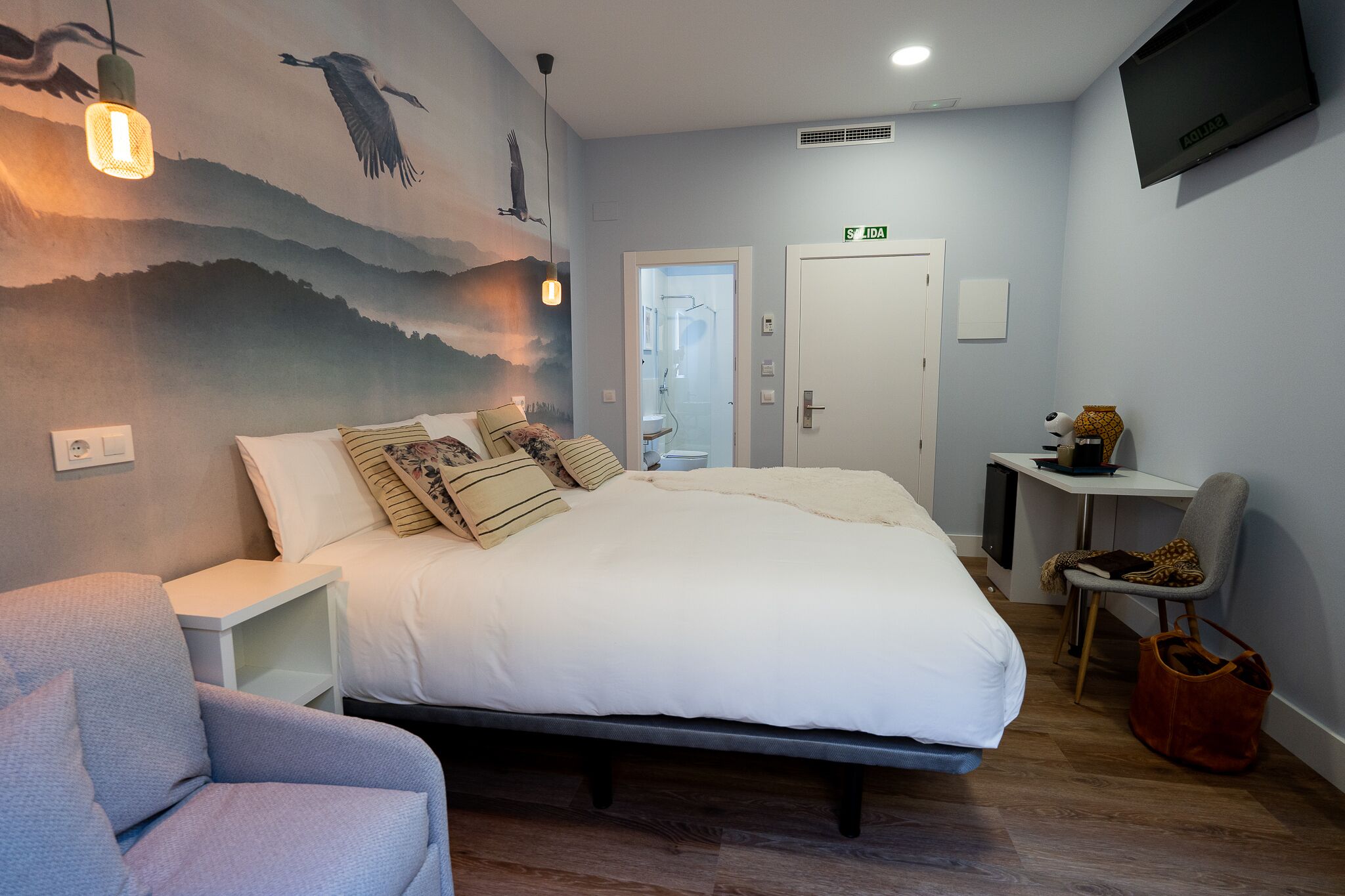 Un dormitorio con cama, mesita de noche, silla, escritorio y televisor.
