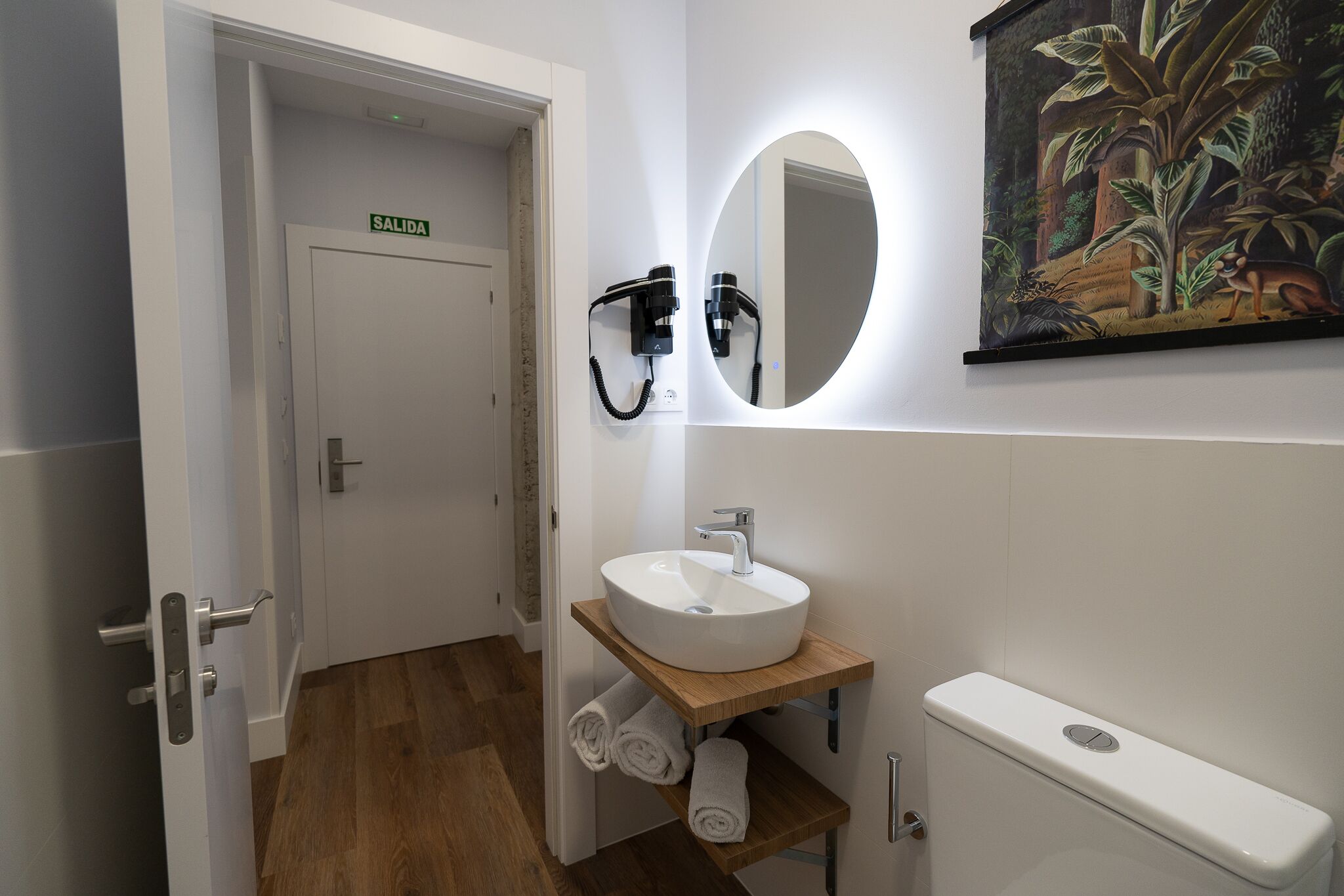A bathroom with a white sink, a toilet, a towel rack, and a mirror with a ring light.