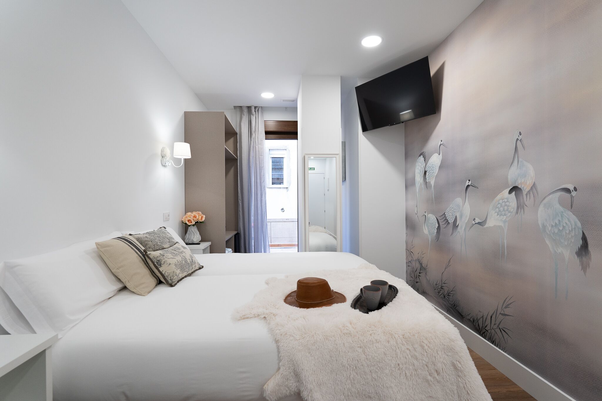 A modern hotel room with a large bed, a flat-screen TV, and a mural of cranes on the wall.
