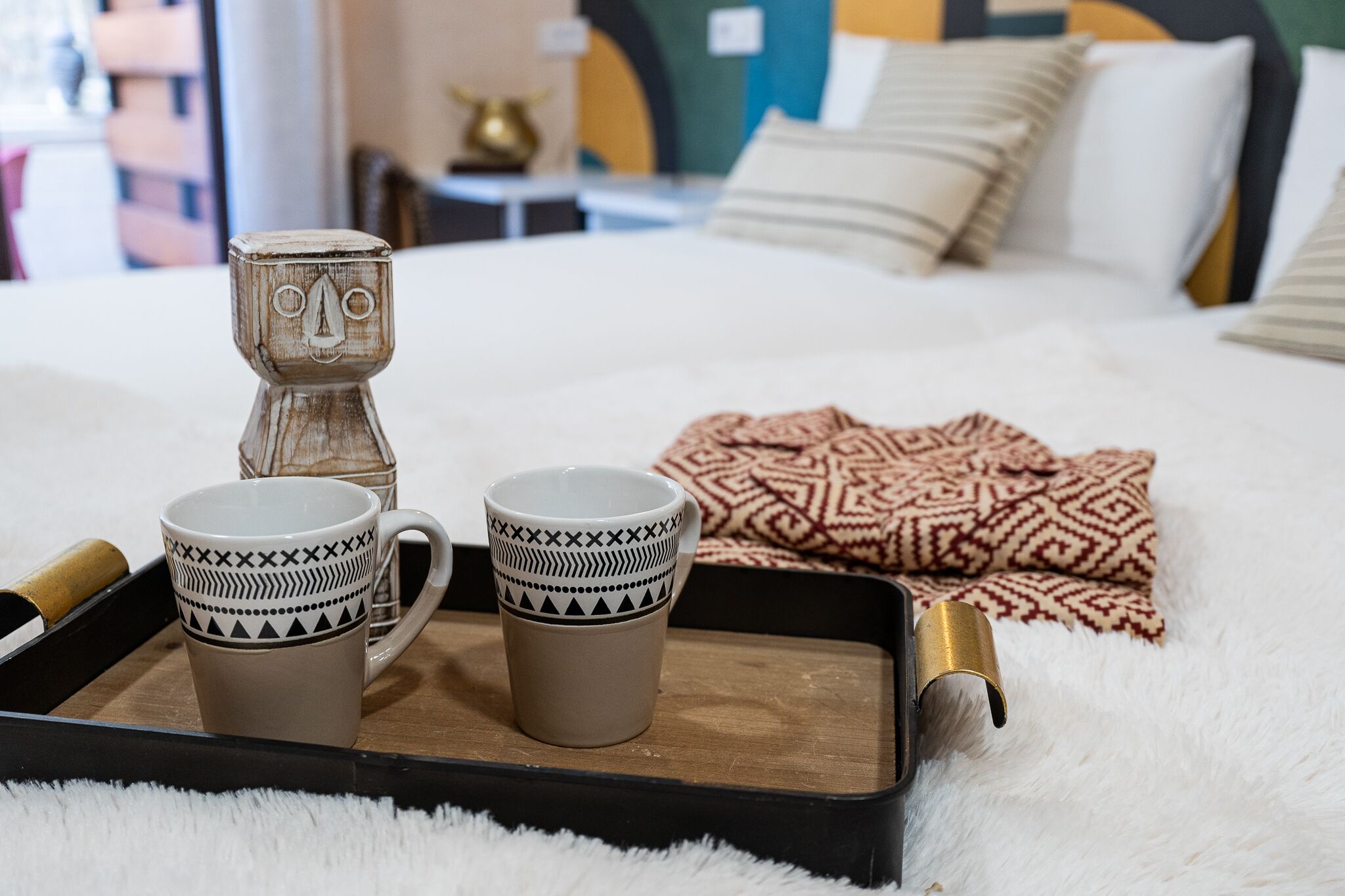 Una cama con un edredón estampado y dos tazas sobre una bandeja.