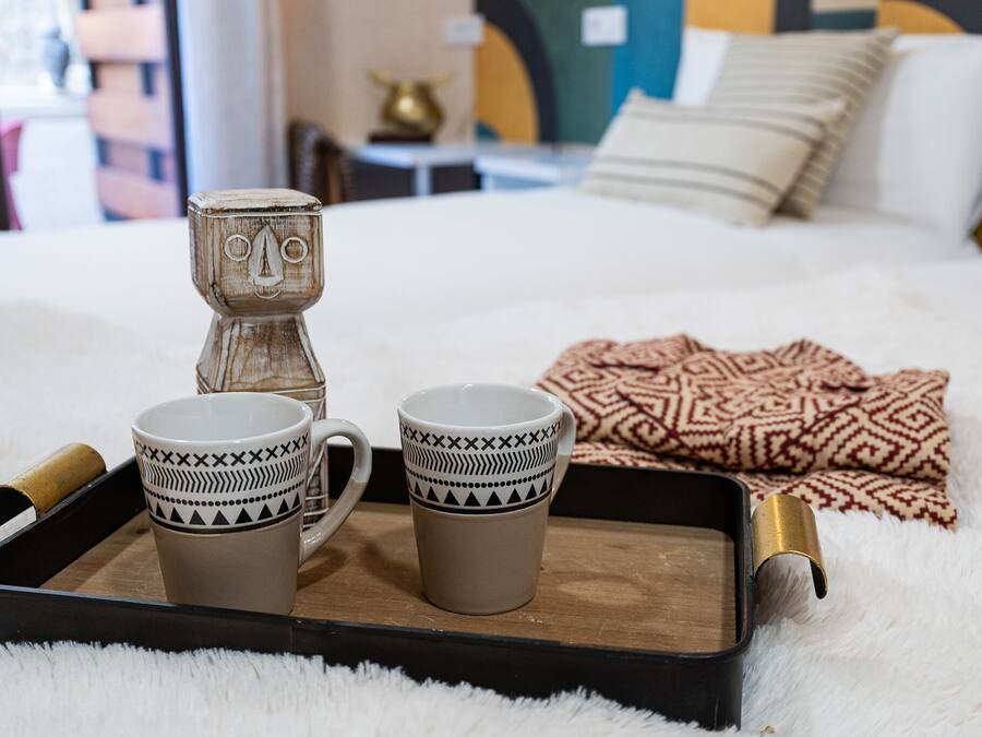 Una cama con un edredón estampado y dos tazas sobre una bandeja.