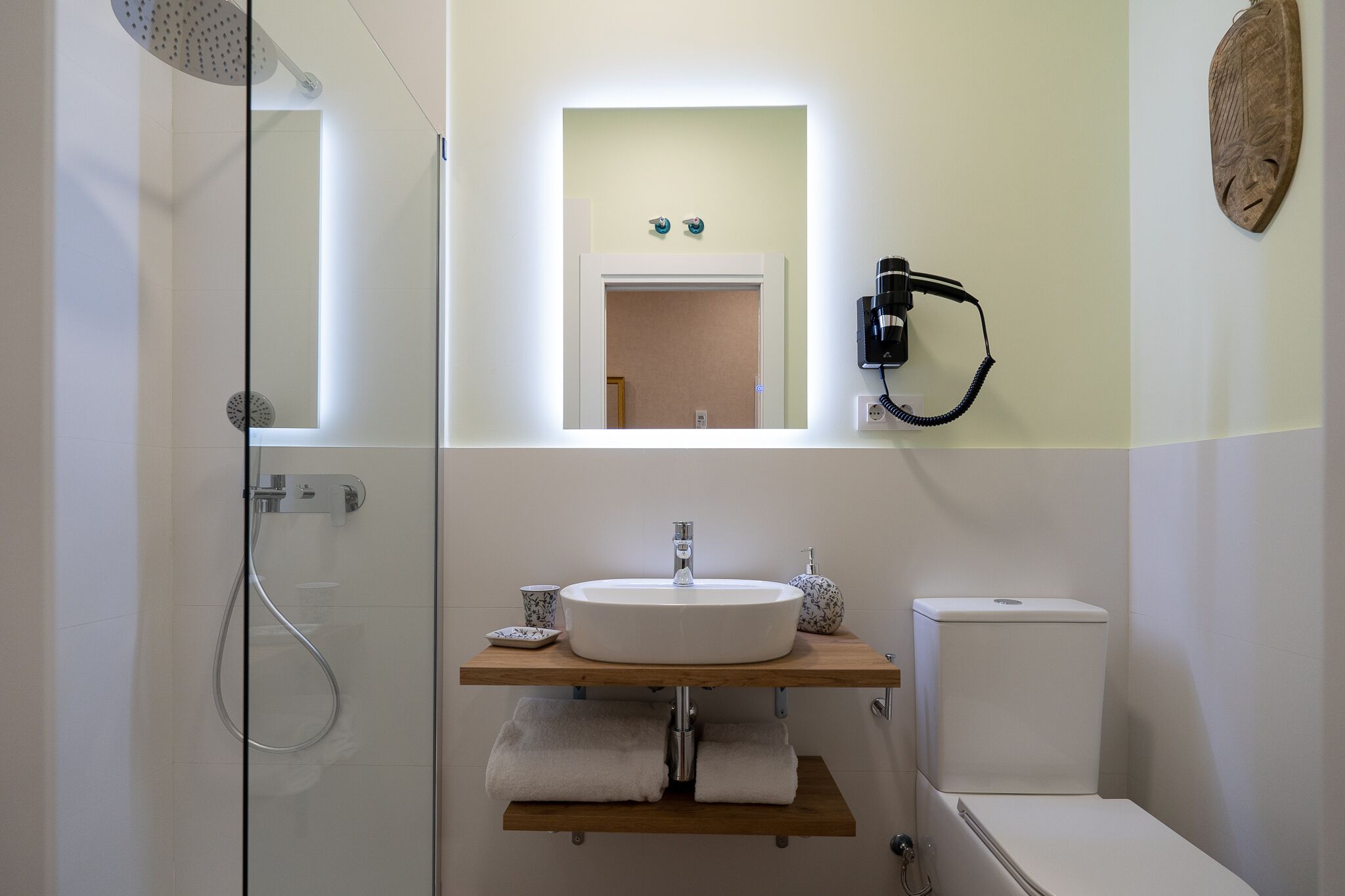 Un baño con cabina de ducha de vidrio, un lavabo blanco con encimera de madera, un espejo y un inodoro.