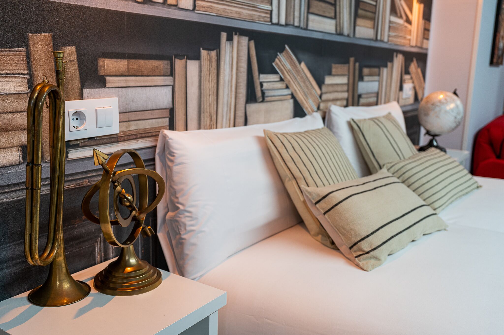 Une chambre à coucher bien rangée, avec un lit blanc, des coussins à rayures et une lampe en laiton posée sur une table de chevet.