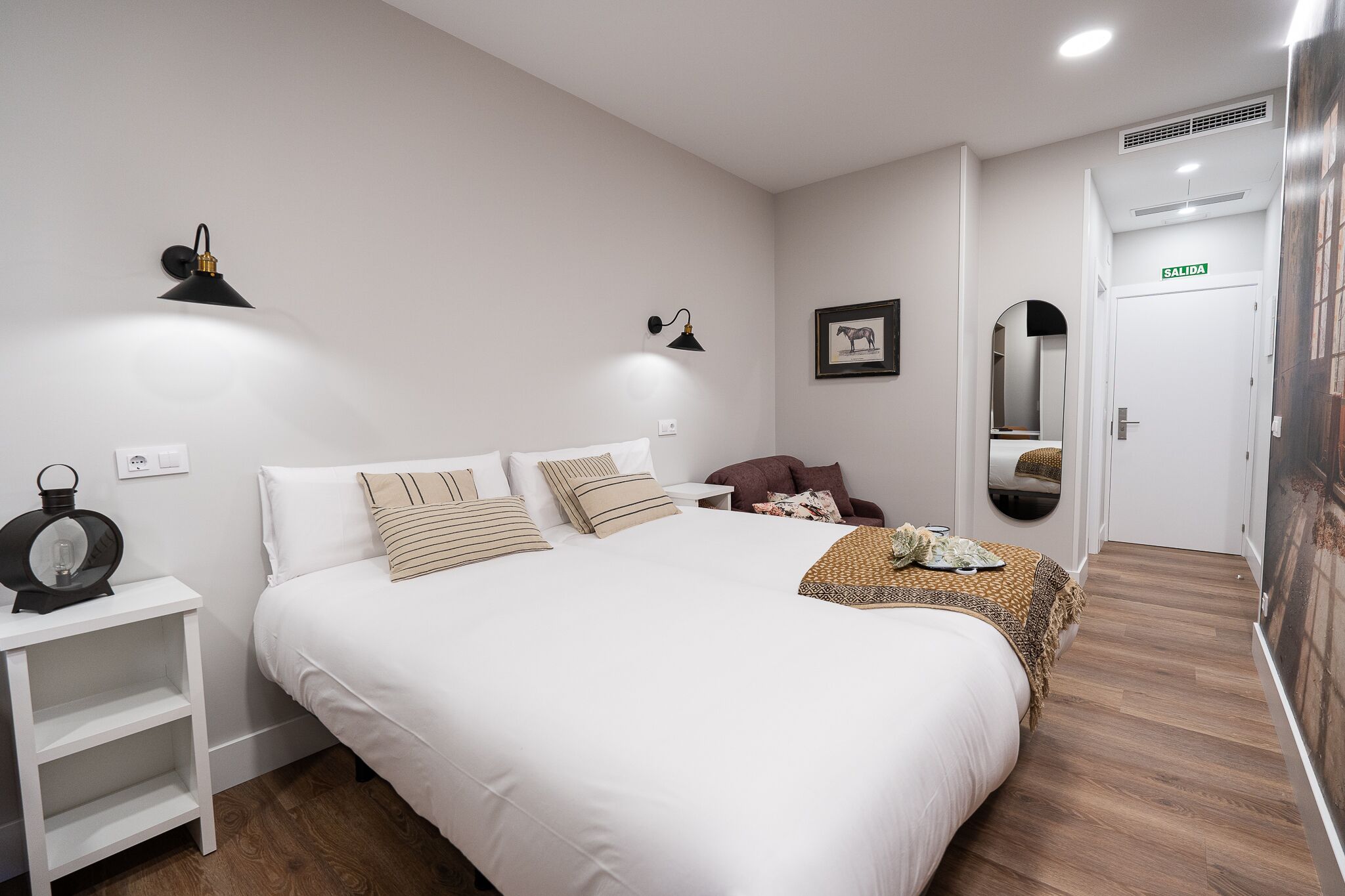 A neatly arranged bedroom with a large bed, bedside lamps, a small table, and a mirror.