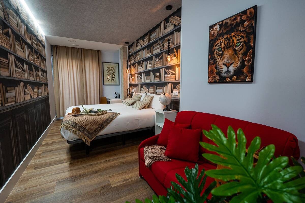 Une chambre avec un grand lit, un canapé rouge, une bibliothèque et un tableau représentant un tigre.