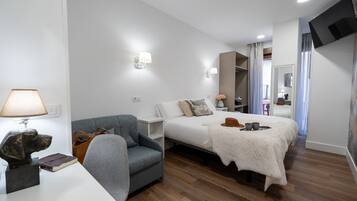 A hotel room with a bed, a chair, a desk with a lamp, and a TV mounted on the wall.