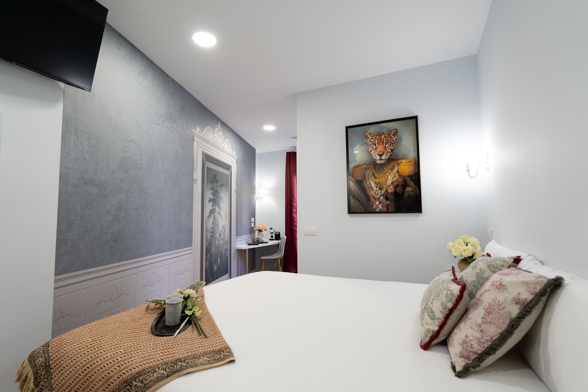 Habitación de hotel con cama, escritorio, silla, televisor y un cuadro de un tigre.