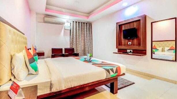 Una habitación de hotel con una cama, televisión montada en la pared, una mesita de noche y un espejo.