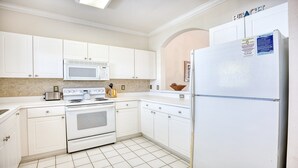 Cocina con alacenas blancas, microondas, estufa y refrigerador.