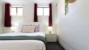 A neatly arranged bedroom with a bed, two bedside tables with lamps, a window with curtains, and a hanging plant. - Riverside Gem with Parking & WiFi (Riverside)