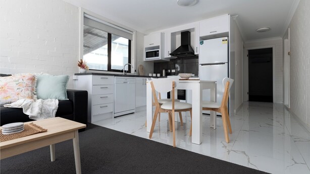 A modern kitchen with white cabinets, a dining area with two chairs, and a black sofa with floral cushions. - Riverside Gem with Parking & WiFi (Riverside)