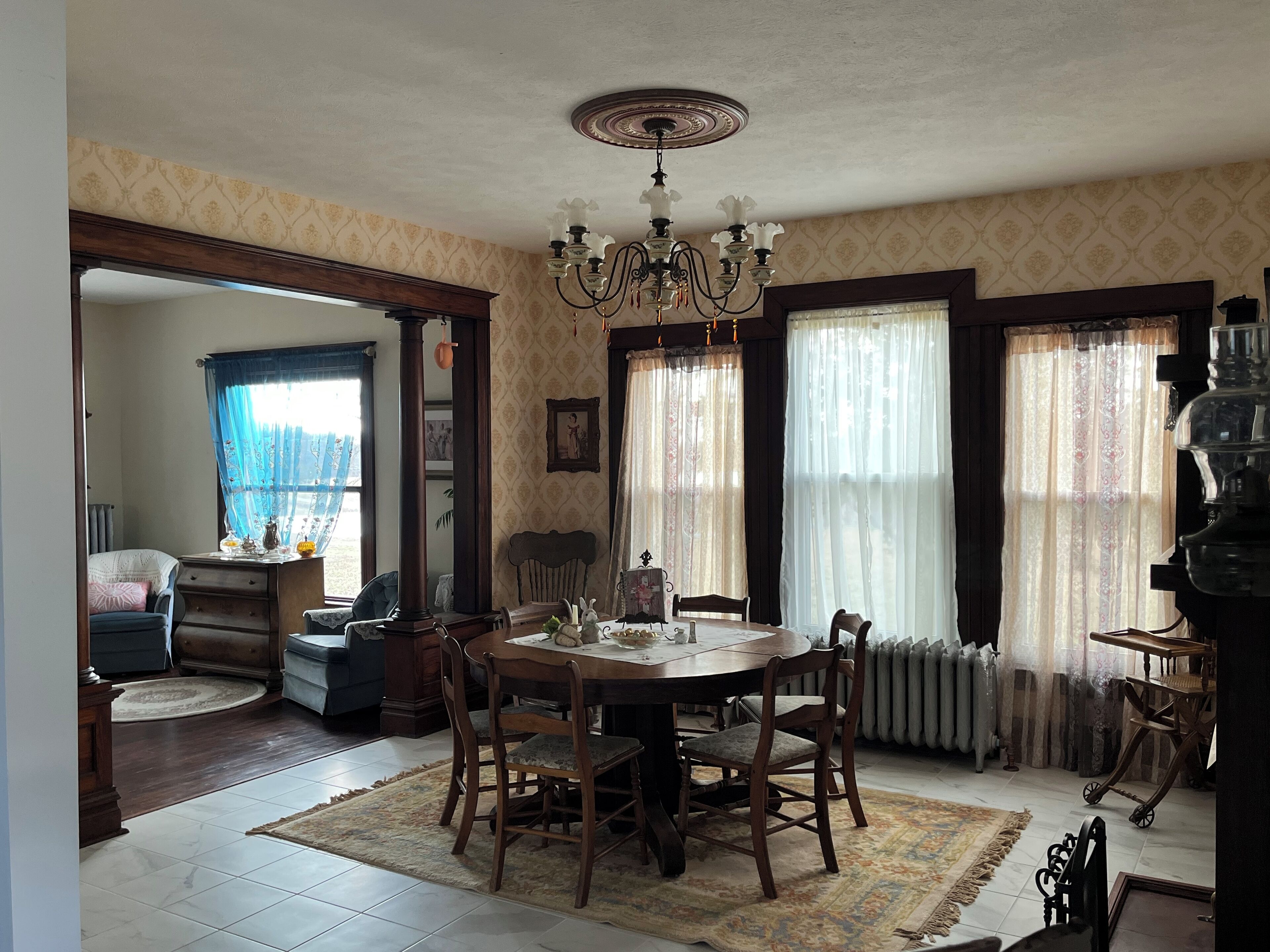 Ein Esszimmer mit Holztisch, Stühlen, einer Chandelierleuchtre und Wandpapier mit Muster.