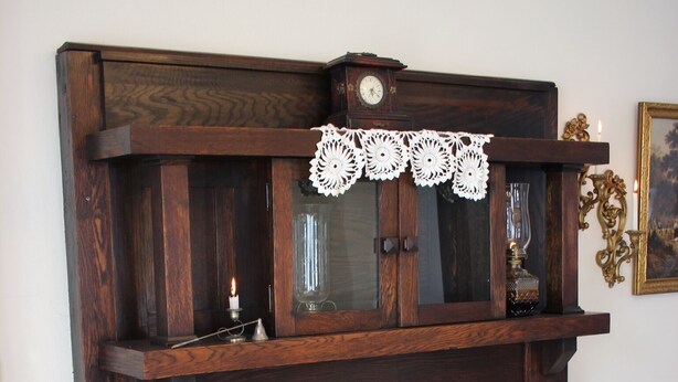 Une cheminée traditionnelle avec un manteau en bois, une nappe en dentelle et des bougies.