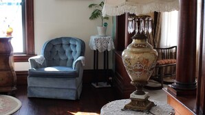 Une pièce avec un fauteuil bleu, un canapé rouge, une lampe de table, un tableau encadré au mur et un plancher en bois.