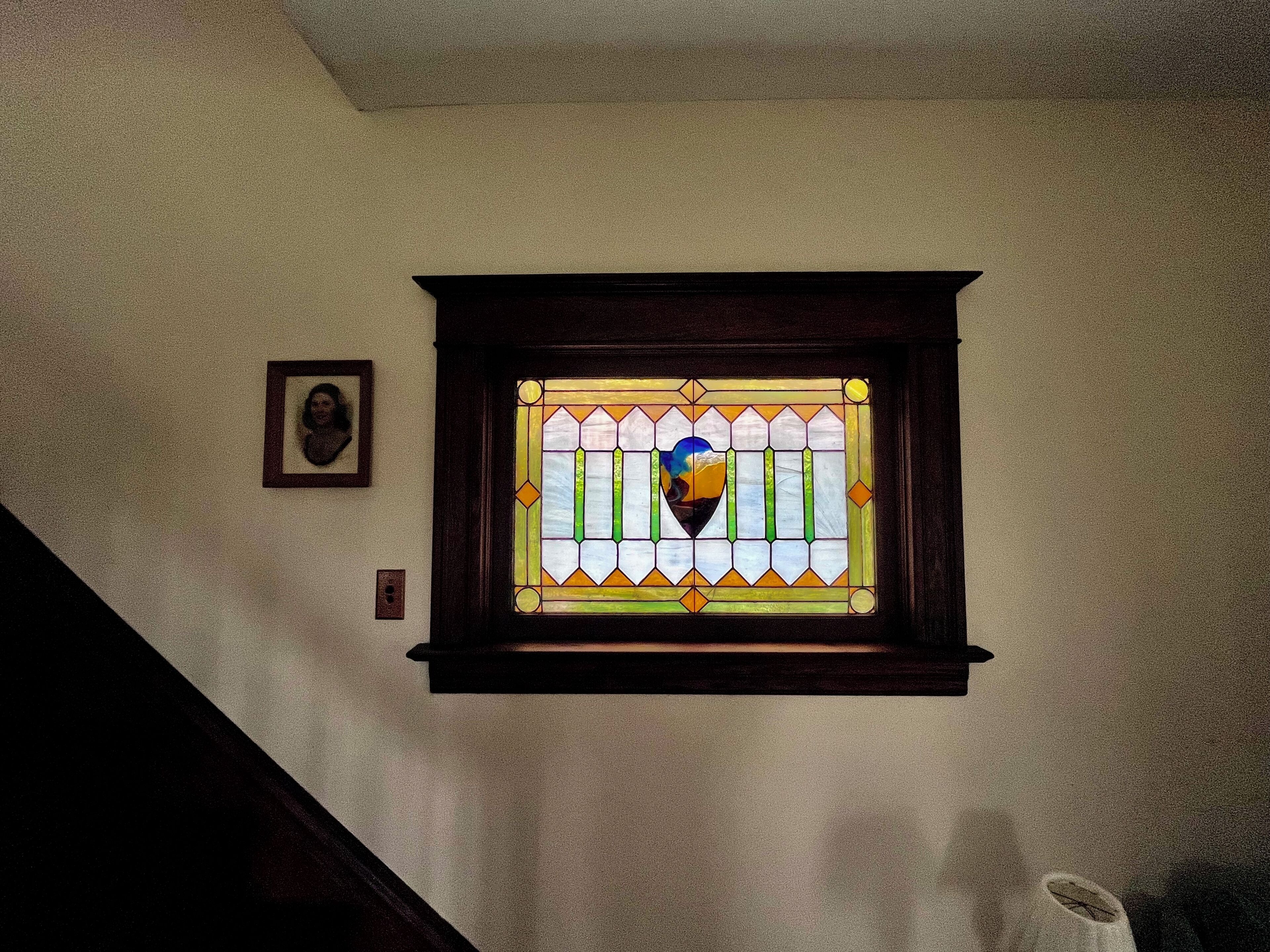 Una ventana de vitral con un diseño de corazón, un cuadro en la pared e interruptor de luz.