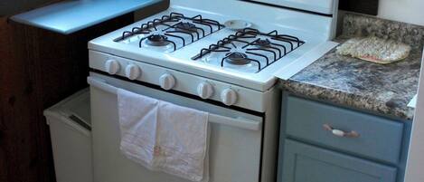 A kitchen with a gas stove, oven, and a small countertop. There is a window above the sink and a rug on the floor.