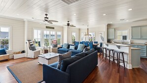 Een ruime woonkamer met een blauwe bank, een salontafel, en een keukenhoek met een bar en barkrukken.