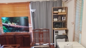 A dining area with wooden furniture, a television, and a kitchen area with appliances. - Elegant Holiday Studio (Werribee)