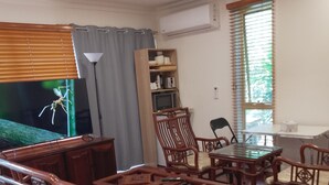 A spacious living room with a wooden dining table and chairs, a television, and a bookshelf. - Elegant Holiday Studio (Werribee)
