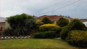 A residential area with a house featuring a red-tiled roof, a white van parked in the driveway, and various well-maintained bushes and plants. - Elegant Holiday Studio (Werribee)