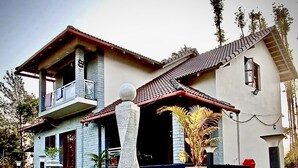 A two-story house with a stone pillar in the front yard, a tiled roof, and a balcony on the upper floor. - Thrilok Vihar (Chikkamagaluru)