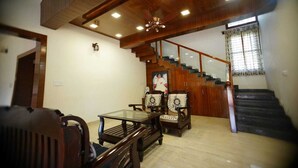 A spacious living room with a wooden staircase, a glass coffee table, and traditional chairs. - Thrilok Vihar (Chikkamagaluru)