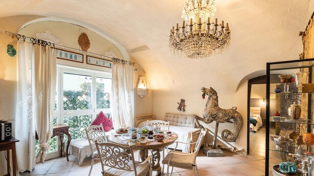 Un espace repas comprenant une table ronde, des chaises, un lustre et une vitrine en verre contenant des objets décoratifs.