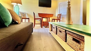 A cozy living room with a sofa, a table, and chairs. A flat-screen TV is mounted on the wall. - Cozy & Whimsical Nautical Theme Walk to Beach & Boardwalk (Wildwood)
