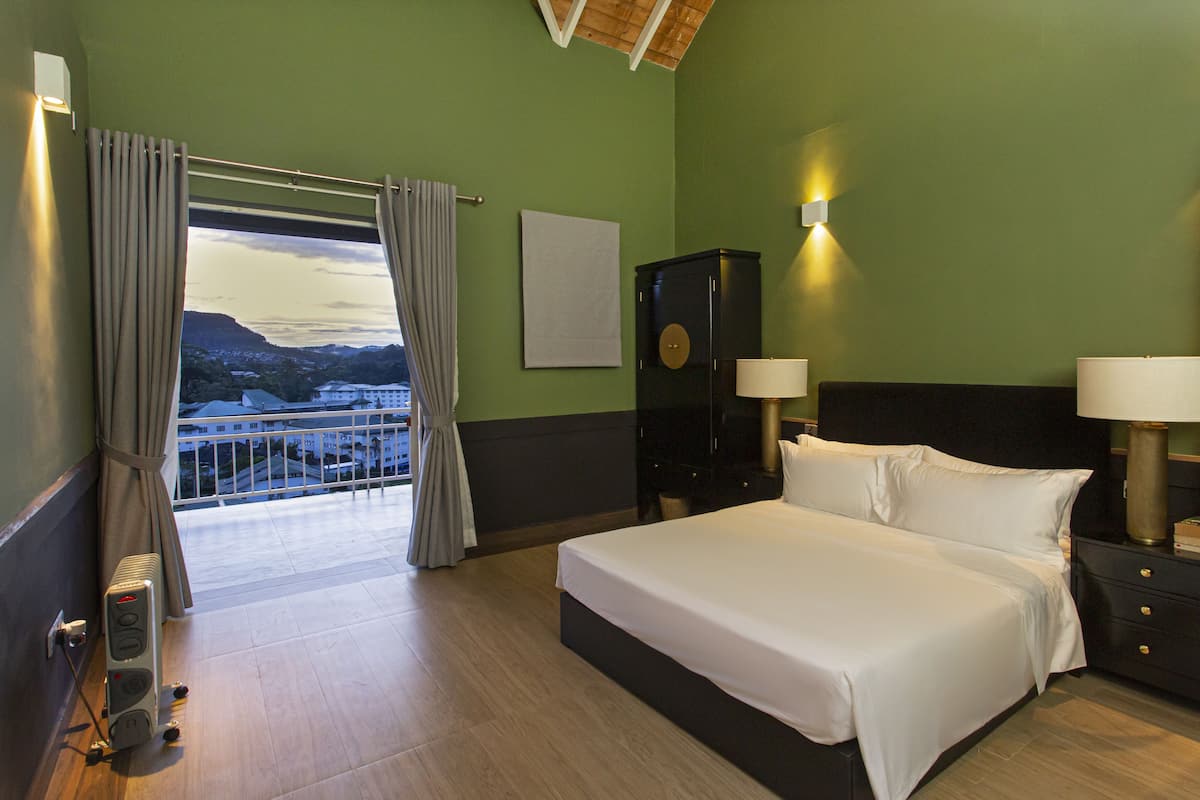 A hotel room with a large bed, two bedside tables with lamps, a dresser, and a view of a mountainous landscape through a large window with curtains.