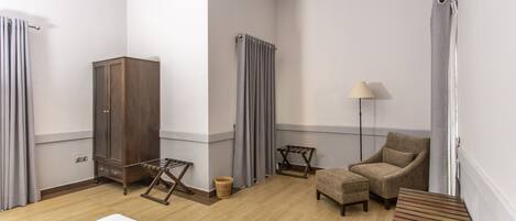 A hotel room with a bed, a wooden bench, a chair, a lamp, a wardrobe, and a radiator.