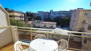 A balcony with a white table and four chairs, overlooking a residential area with buildings and trees. - Cozy Apartment with Terrace Overlooking Pool in Vibrant Salou (Salou)