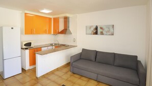 A compact kitchen with a refrigerator, microwave, and orange cabinets, a gray sofa, and a tiled floor. - Cozy Apartment with Terrace Overlooking Pool in Vibrant Salou (Salou)