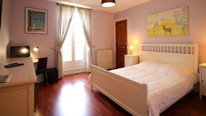 Ein Schlafzimmer mit einem Bett, einem Schreibtisch, einem Stuhl, einer Lampe, einem Heizkörper und einem Bild an der Wand.