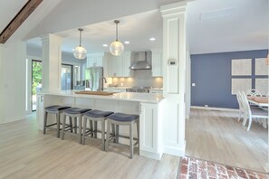 A modern kitchen with a central island, bar stools, pendant lighting, and a dining area with a table and chairs.