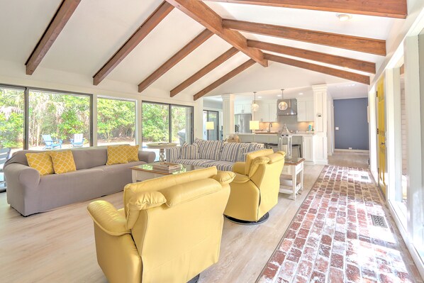 A spacious living area with a sofa, yellow armchairs, and a striped couch. A kitchen is visible in the background.