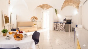 A modern living room with a sofa, a dining table with breakfast items, and a kitchen area with a microwave and sink. - Home Studio Oneglia (Imperia)
