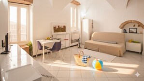 A bright living room with a sofa, a dining area with a table and chairs, and a kitchen area with a fridge and a sink. - Home Studio Oneglia (Imperia)
