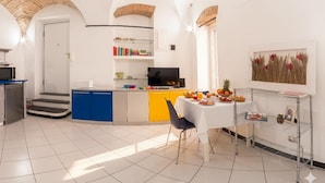 A modern kitchen with a central island, a dining area with a white table, and a TV on a shelf. - Home Studio Oneglia (Imperia)