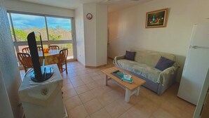 A living room with a sofa, a coffee table, a TV, and a dining area with chairs and a table. - Cozy T2 Apartment with Parking, Pool, and City View Near Beach in Argelès-sur-Mer (Argelès-sur-Mer)