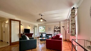 A spacious living room with a wooden parquet floor, a ceiling fan, a television, and a bookshelf. - Spacious 4-Room Apartment with Garden & Parking - Sleeps 6, Briançon (Briançon)