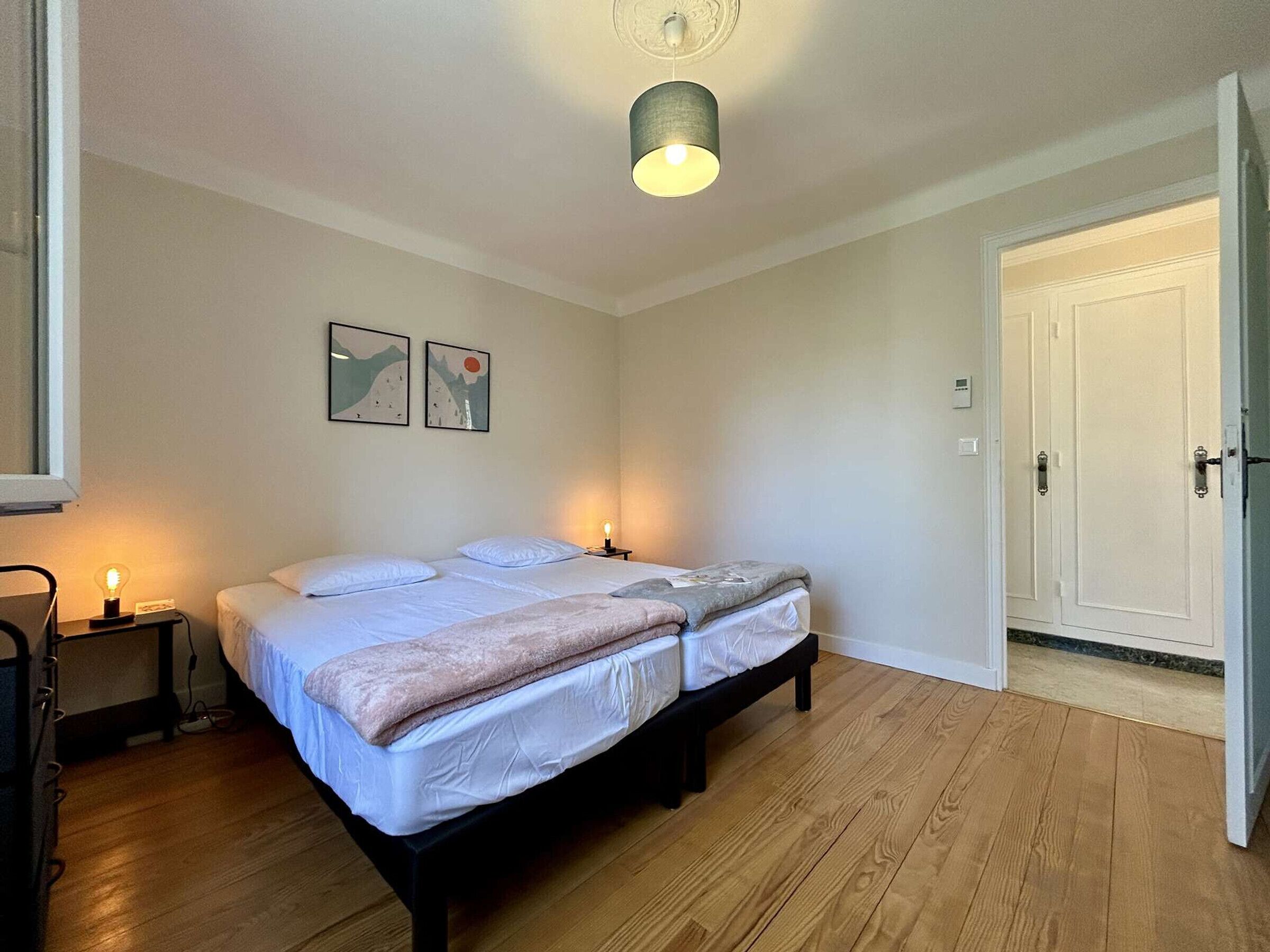 A bedroom with a double bed, bedside tables, a ceiling light, and two framed pictures on the wall.